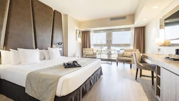 Habitación de hotel con una cama grande, un escritorio con silla, un comedor y un amplio ventanal con vistas.