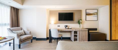 A modern hotel room with a bed, a desk, a chair, a TV, and a painting on the wall.