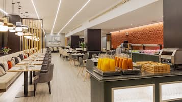 A modern dining area with long tables, chairs, and a buffet counter with food and drinks.