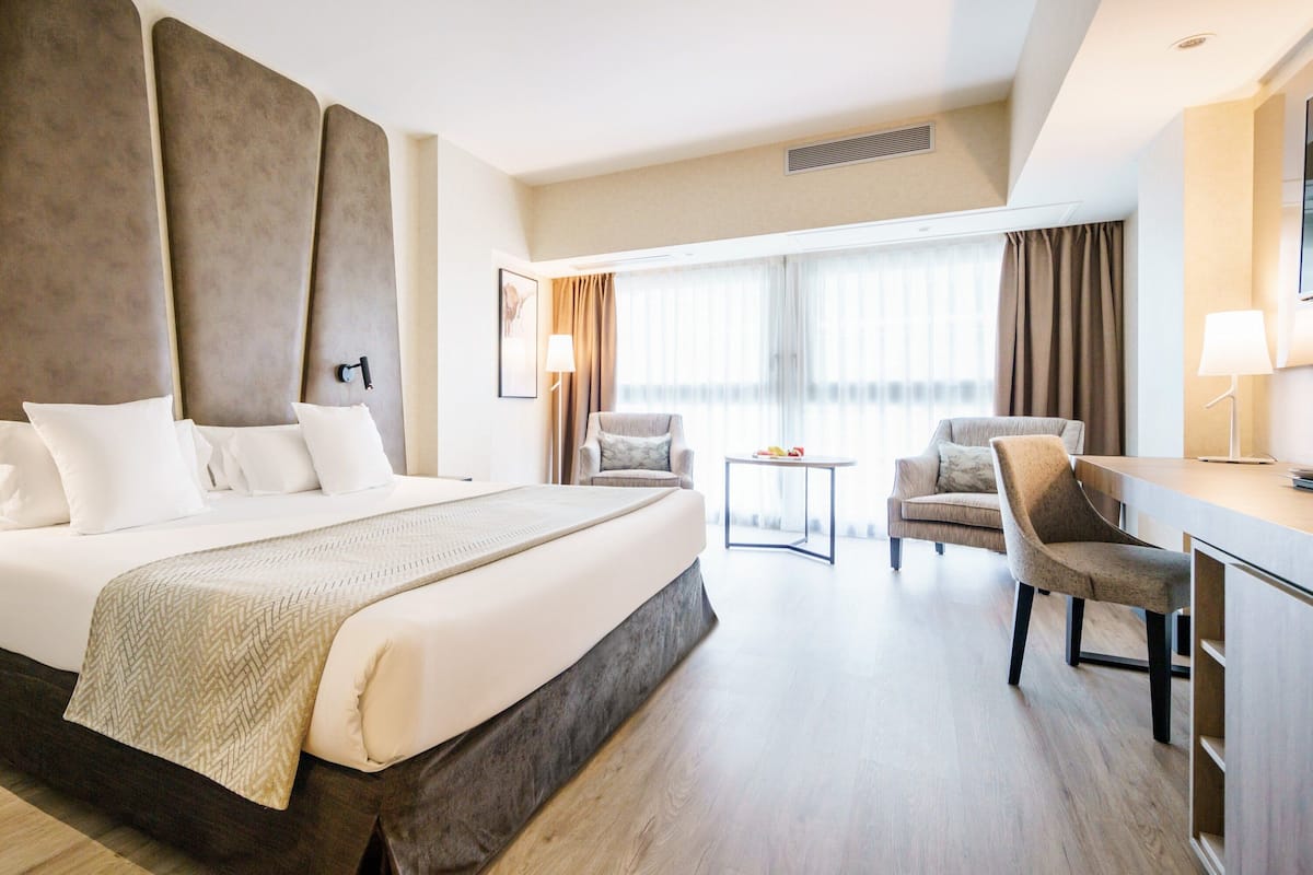 Una habitación de hotel con una cama grande, dos sillones, una mesita y un escritorio con lámpara.