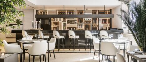 Zona de bar moderna con una barra larga, diferentes opciones de asientos y una variedad de botellas y copas.