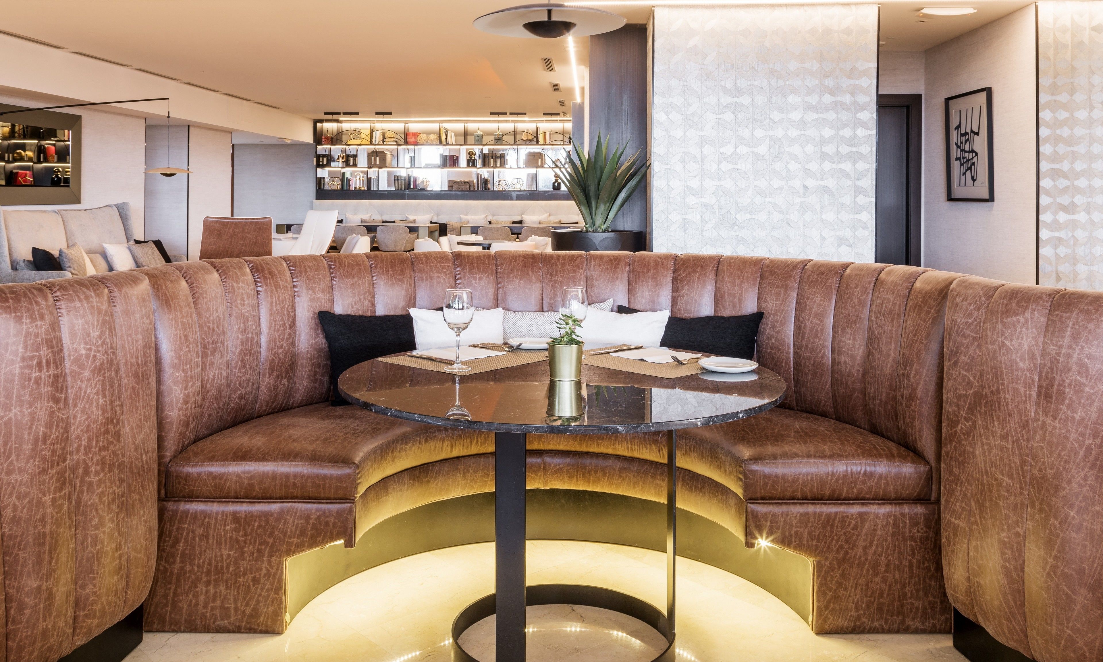 A modern, curved seating area with a glass table, surrounded by plush, brown leather sofas.