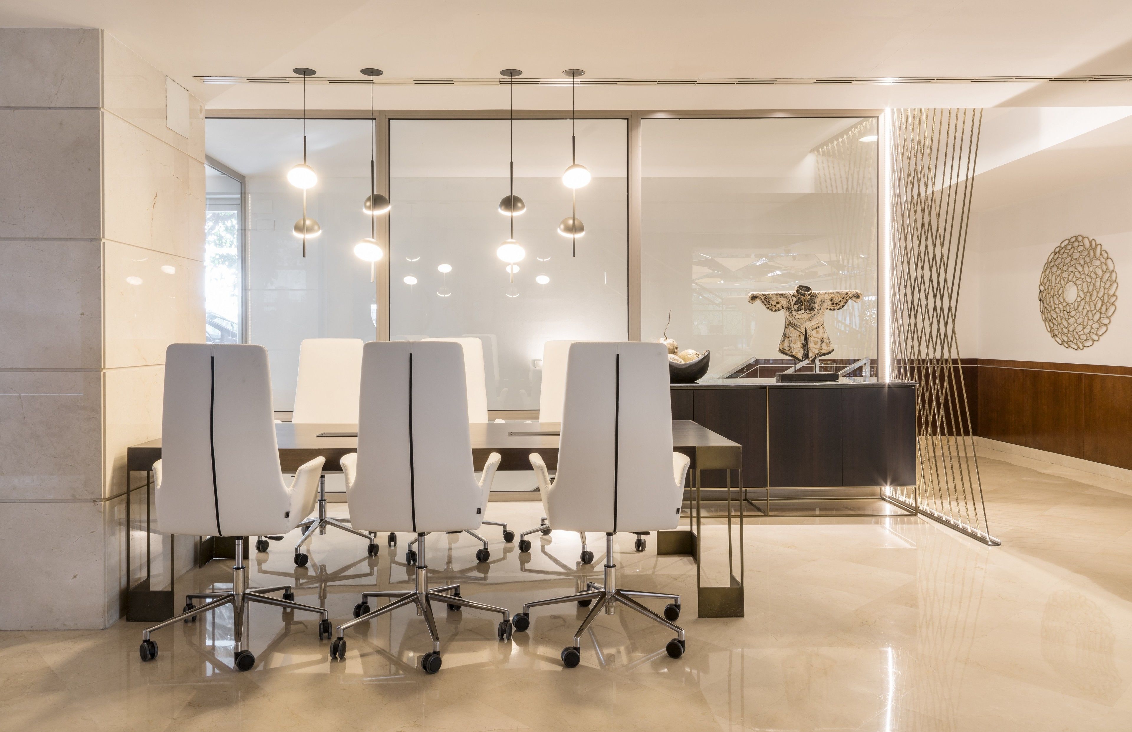 Une salle de conférence moderne dotée d’une cloison en verre, de chaises blanches, d’une table centrale et d’un éclairage suspendu.