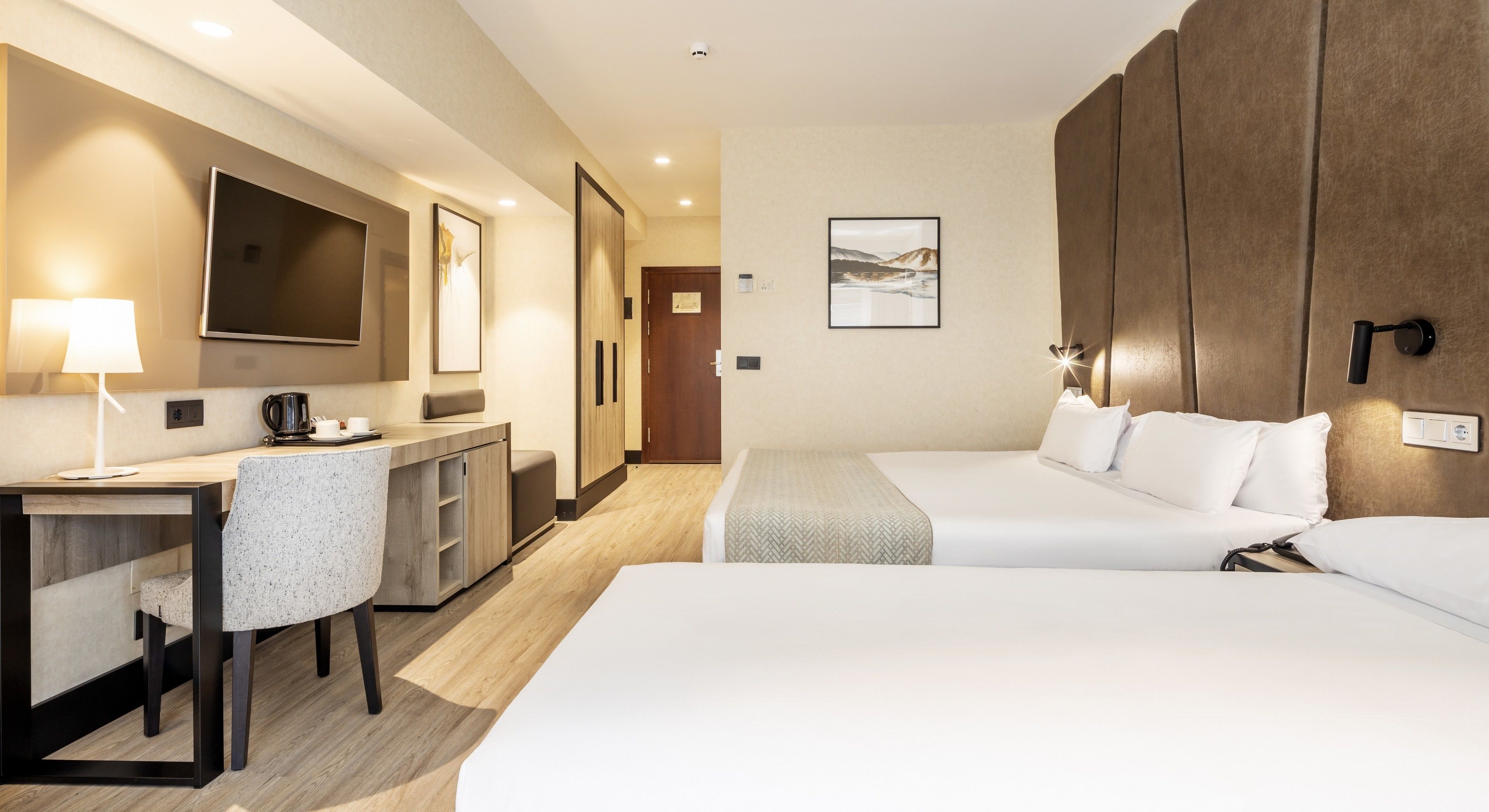 Habitación de hotel con escritorio, dos camas, televisión y un cuadro en la pared.