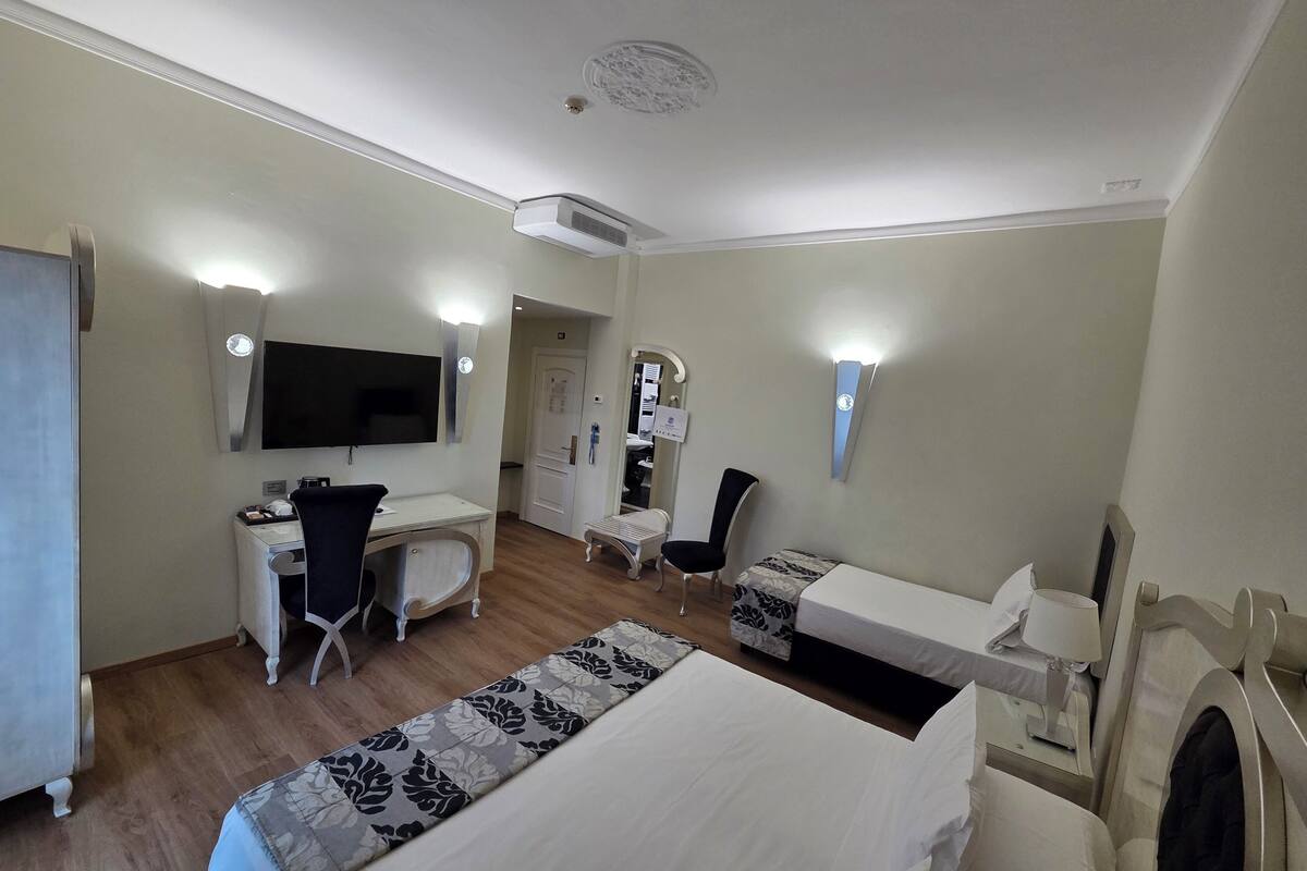 Habitación de hotel con cama, escritorio, silla, televisor y aire acondicionado instalado en la pared.