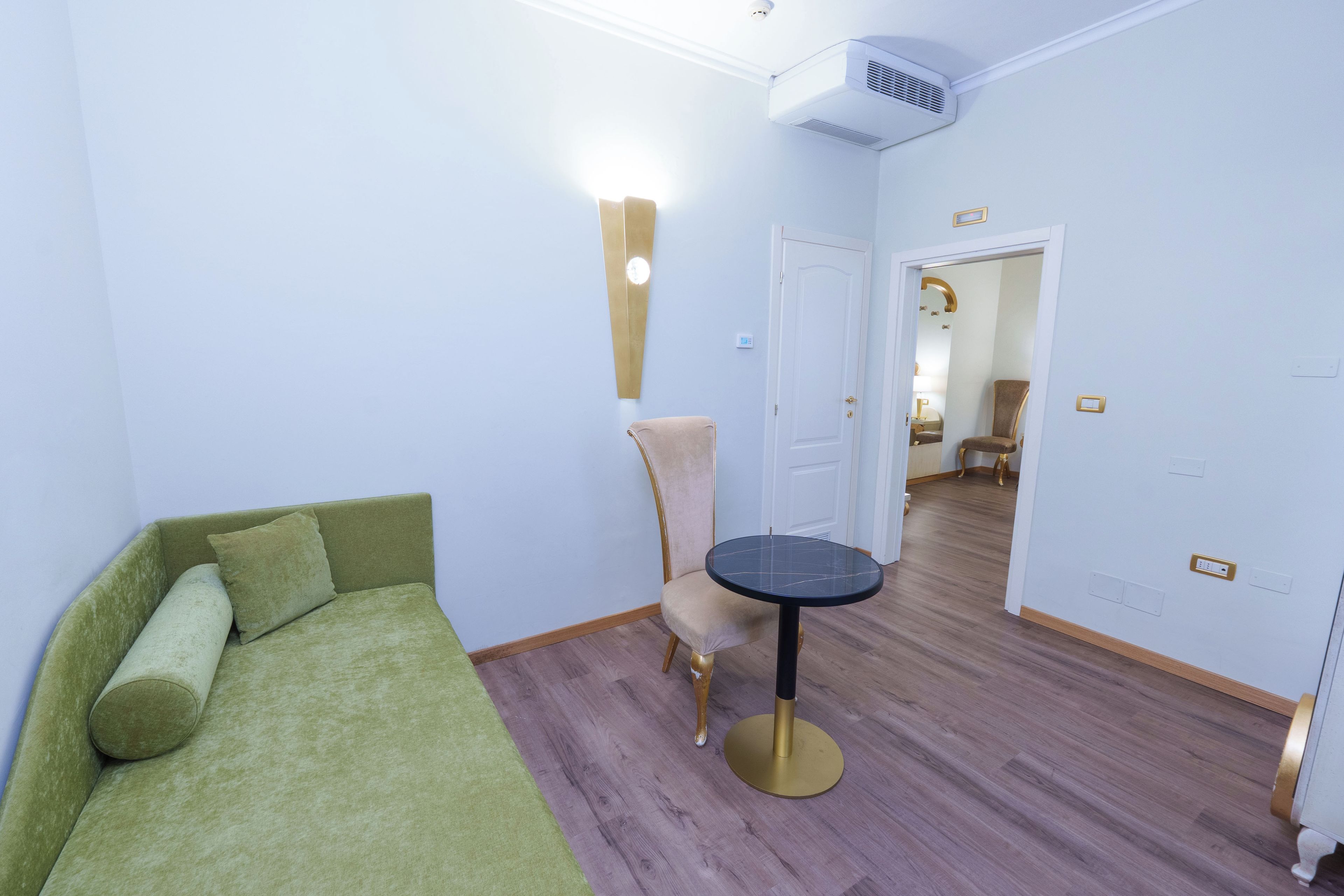 A room with a green sofa, a round table, a chair, and a door leading to another room.