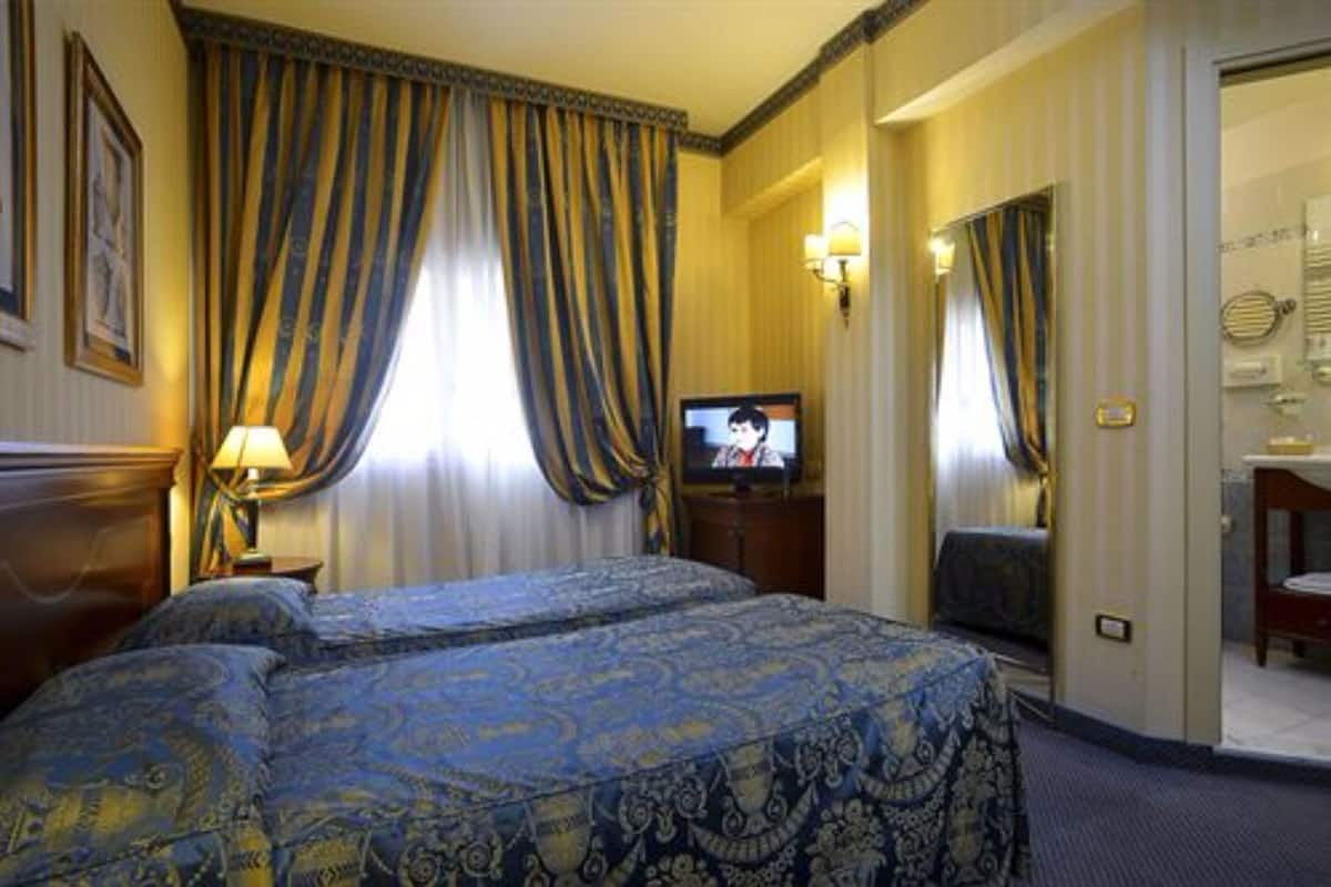 Habitación de hotel con dos camas, un televisor y un baño visible a través de una puerta abierta.