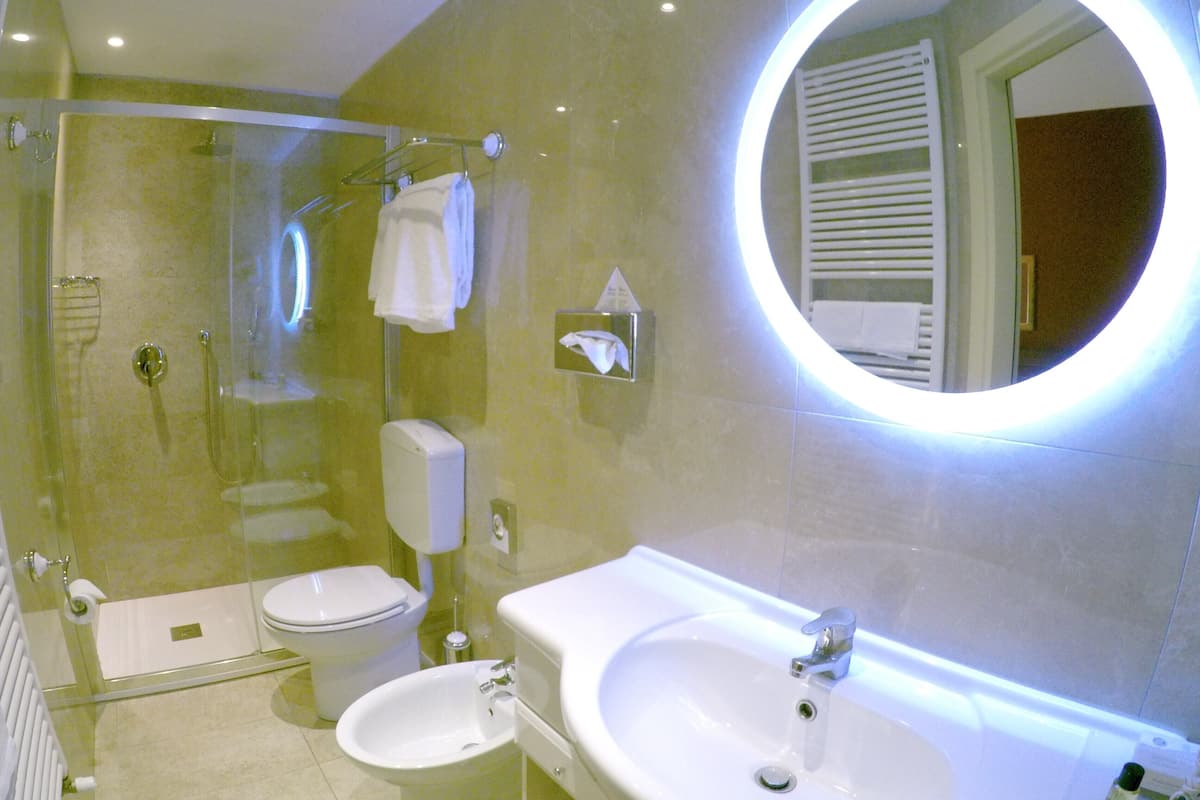Un baño moderno con ducha de vidrio, inodoro, bidé y lavabo con espejo arriba.