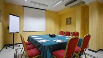 Ein Konferenzraum mit großem Tisch, roten Stühlen, einer Projektionsleinwand und einer Whiteboard-Tafel.