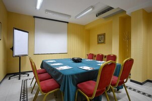 Een vergaderzaal met een grote tafel, rode stoelen, een projectiescherm en een whiteboard.