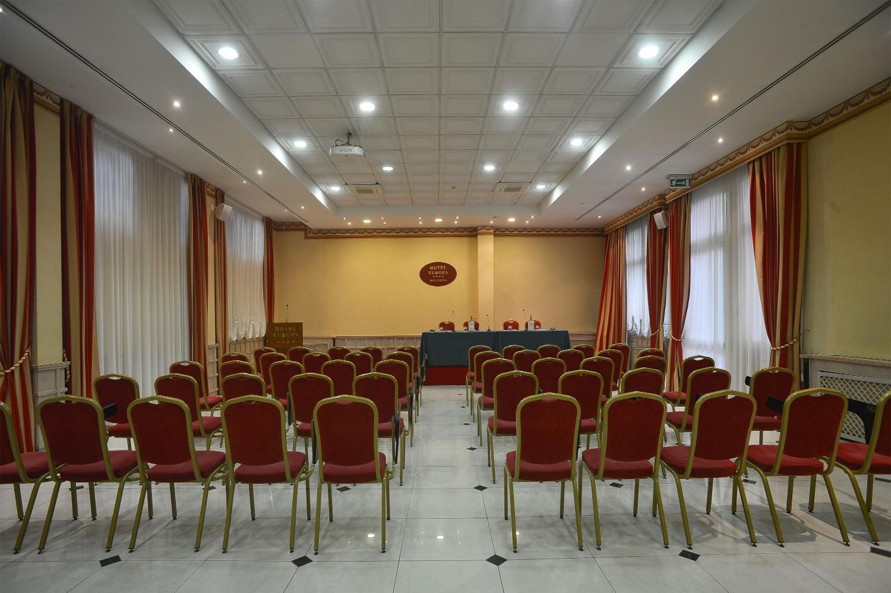 A conference room with rows of red chairs, a podium, and a sign indicating 'HOTEL EUROPA.'