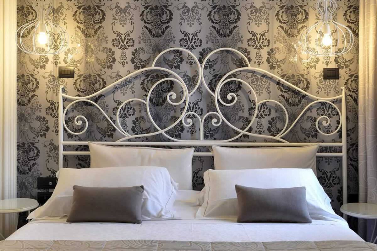 A neatly made bed with a white metal headboard, white bedding, and two bedside tables with lamps.