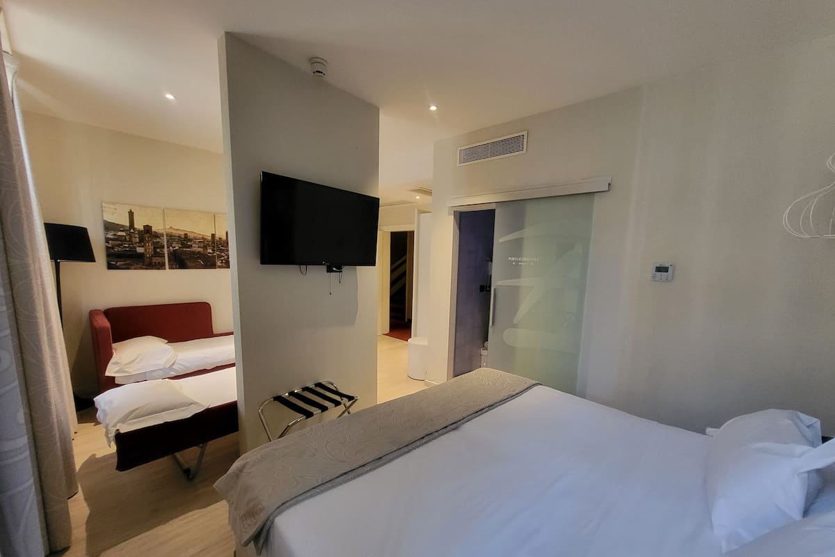 A hotel room with a bed, a red chair, a TV mounted on the wall, and a wardrobe with a mirror.