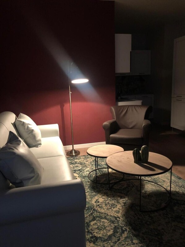 Una sala de estar con un sofá, un sillón, dos mesas auxiliares, una lámpara de pie y un tapete estampado.