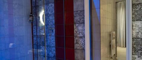 A modern bathroom with a glass shower enclosure, a large mirror, and a small stool.