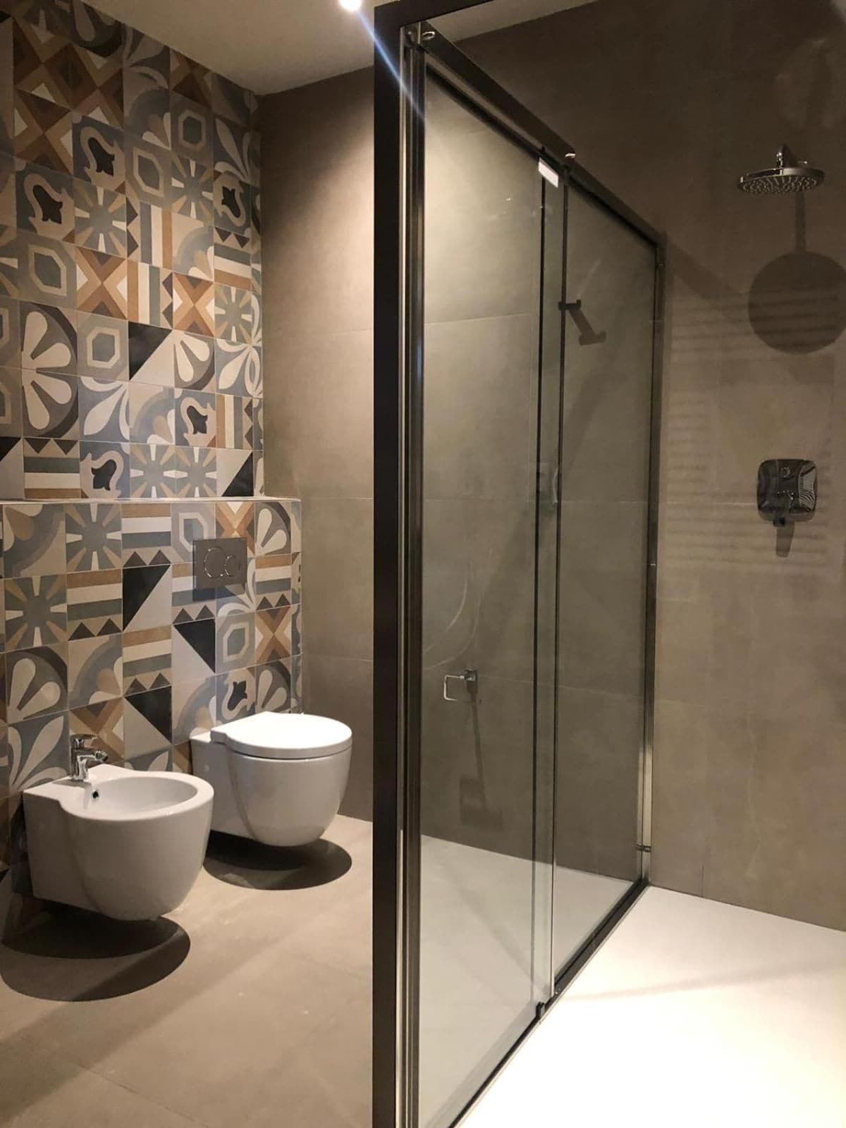 Een moderne badkamer met een douche met glazen wand, een toiletbrons en een toilet.