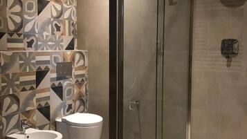 Een moderne badkamer met een douche met glazen wand, een toiletbrons en een toilet.