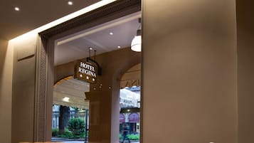 A hotel lobby with a leather sofa, a white ottoman, and a wooden bench. A sign indicates the hotel name.