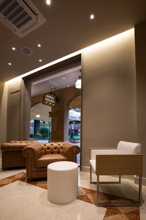 A hotel lobby with a leather sofa, a white ottoman, and a wooden bench. A sign indicates the hotel name. - Zanhotel Regina (Bologna)