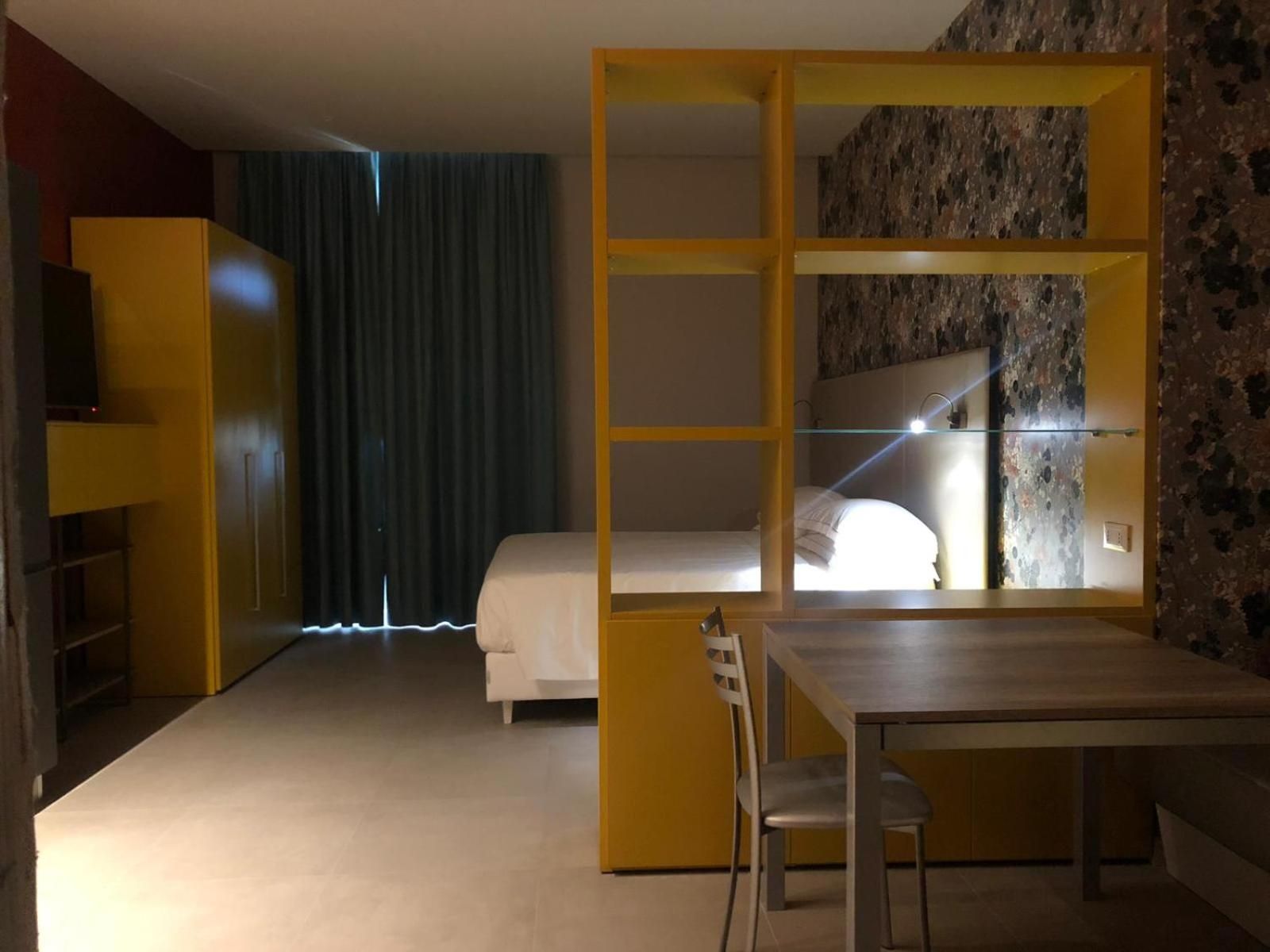 Quarto com uma cama, uma escrivaninha e uma cadeira. Possui um guarda-roupa e um espelho na parede.
