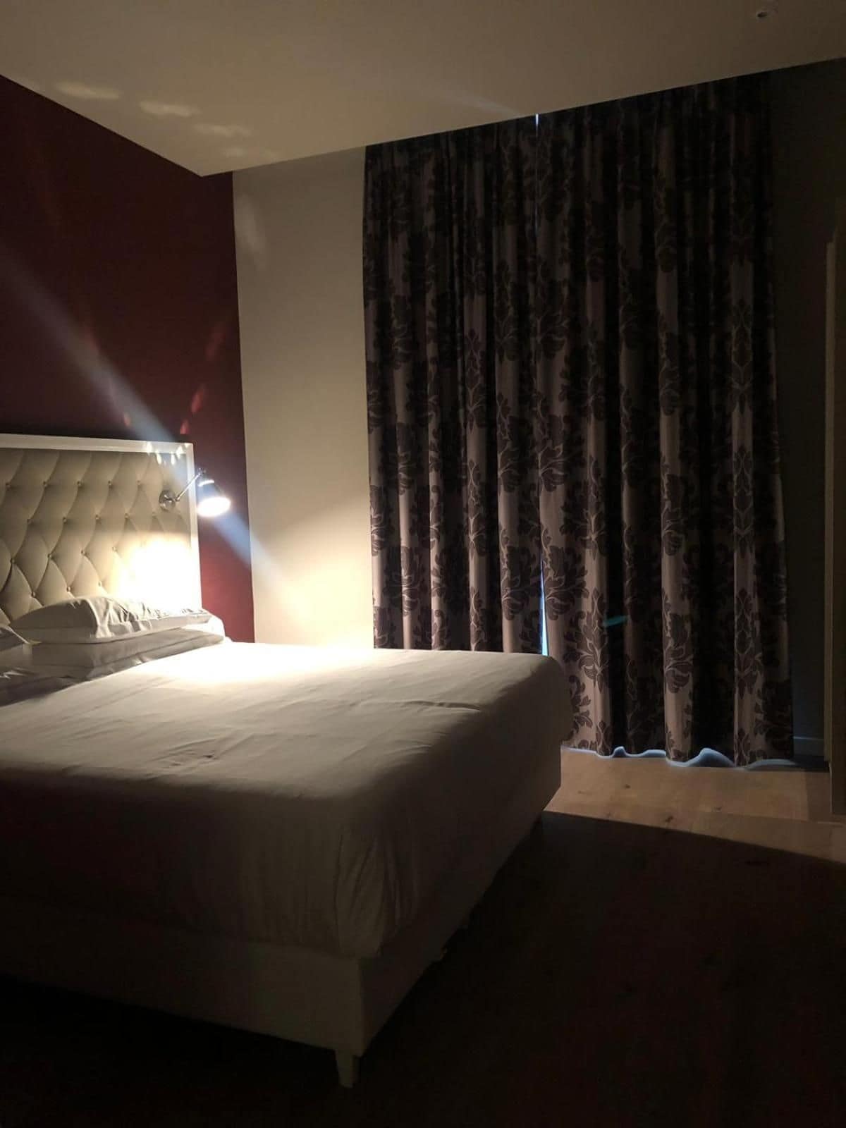 A hotel room with a large bed, a tufted headboard, and a window with curtains.