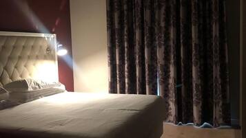 A hotel room with a large bed, a tufted headboard, and a window with curtains.