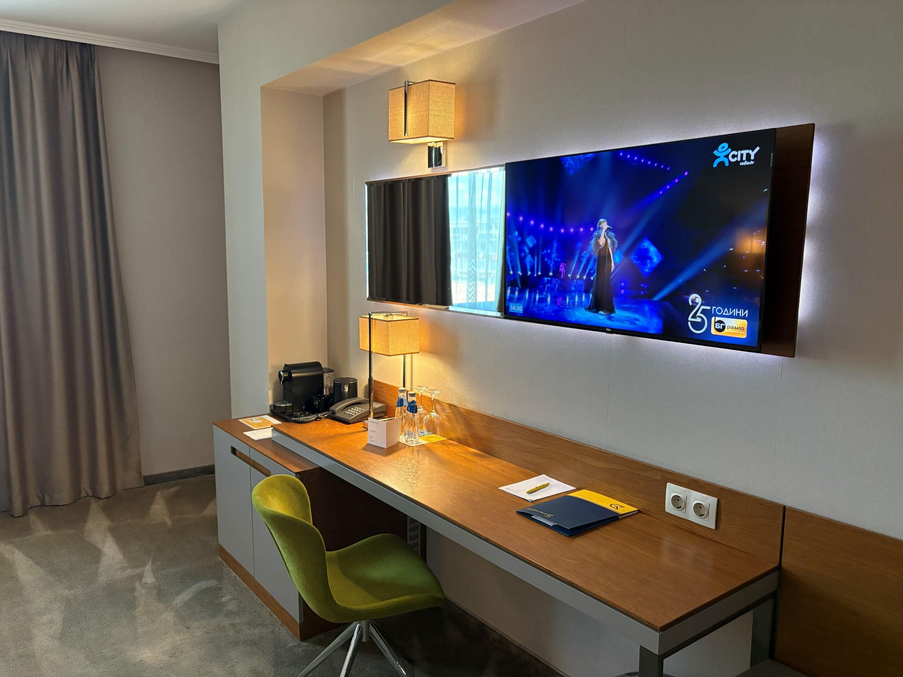 Een hotelkamer met een bureau, stoel, televisie, lamp en een koffiezetapparaat.