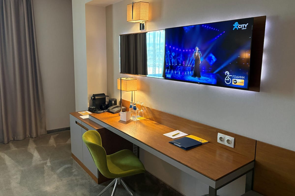 A hotel room with a desk, chair, TV, lamp, and a coffee maker.