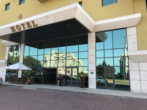 Entrada de hotel con fachada de vidrio, asientos exteriores y una vista despejada de los edificios circundantes.