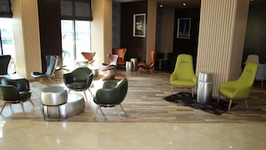 A spacious lobby with modern seating arrangements, including leather and green chairs, and a polished marble floor. - Golden Tulip Varna (Varna)