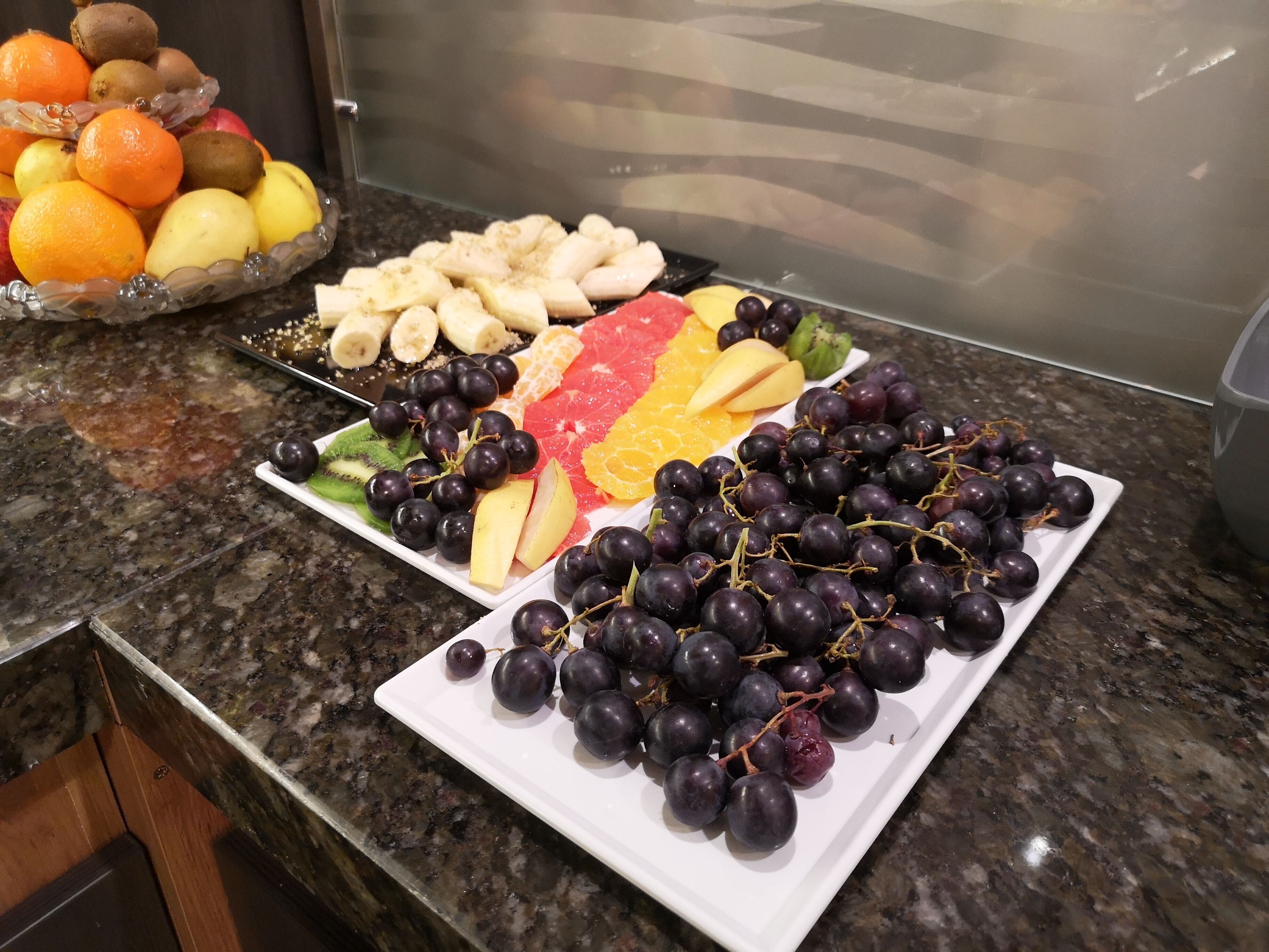 Una encimera de cocina con una bandeja de frutas que incluye uvas, naranjas y otras frutas.