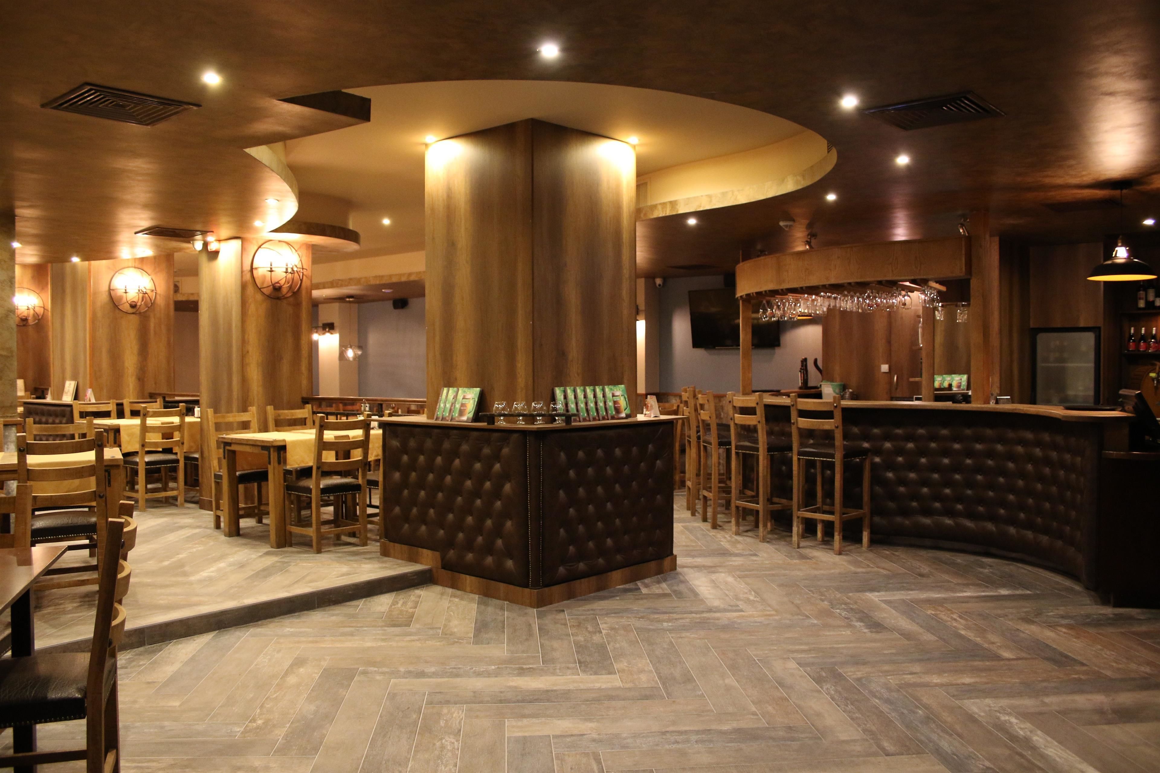 A restaurant interior with wooden furniture, a central bar area, and a herringbone floor pattern.
