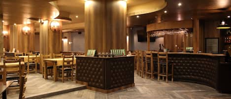 A restaurant interior with wooden furniture, a central bar area, and a herringbone floor pattern.