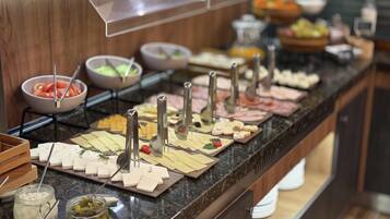 A buffet with various cheeses, meats, and condiments.