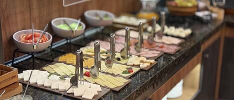 A buffet with various cheeses, meats, and condiments.
