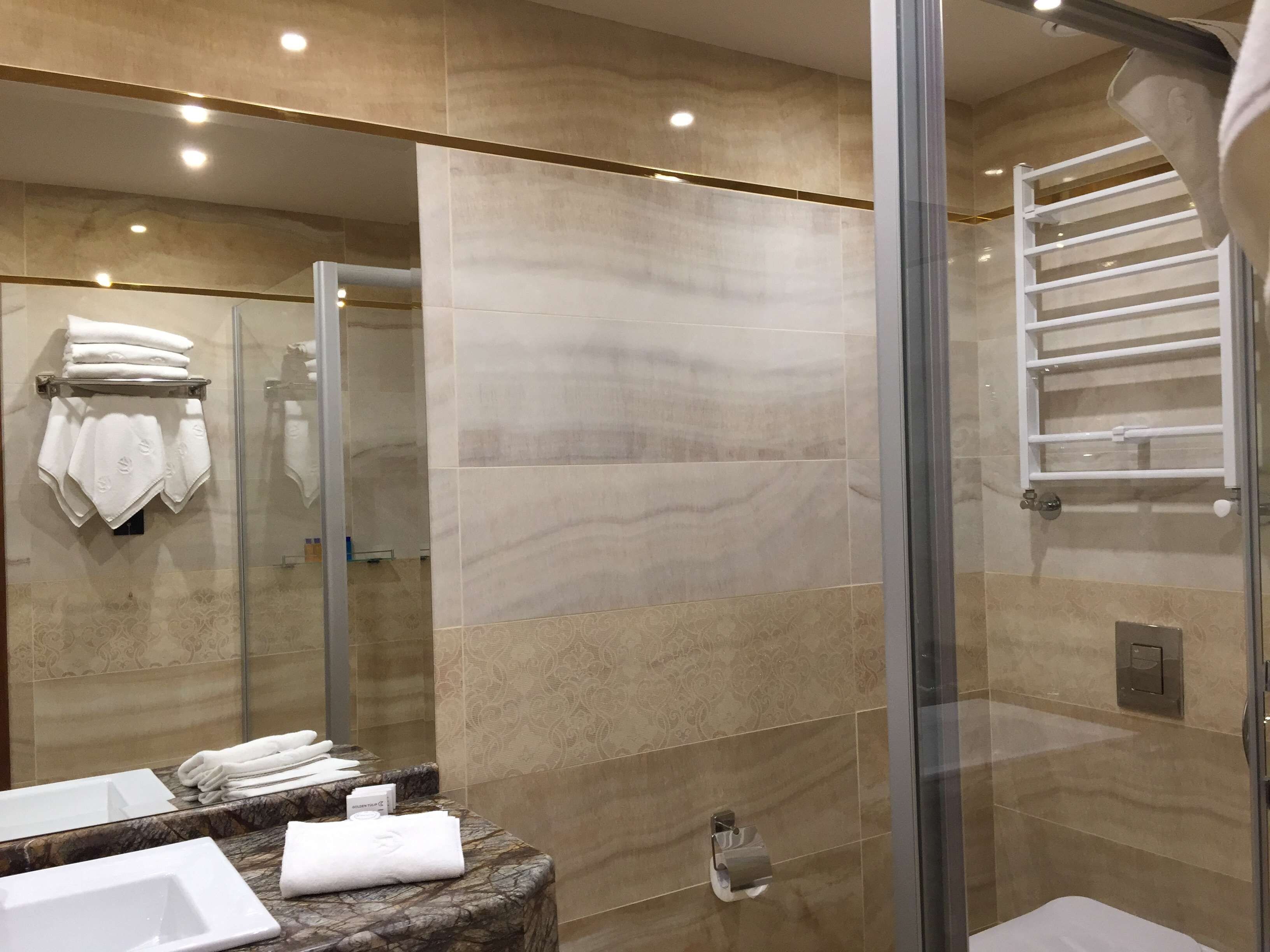 Un baño moderno con cabina de ducha de vidrio, encimeras de mármol y un perchero para toallas.