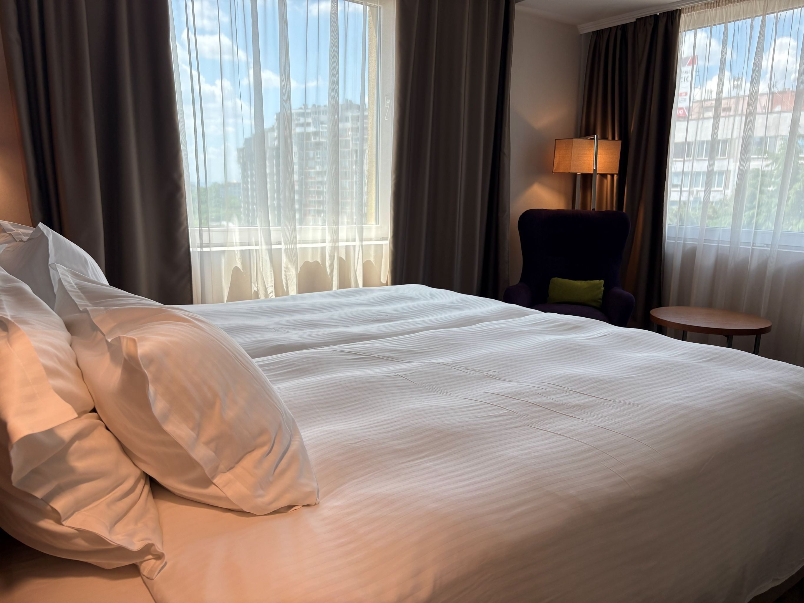 A hotel room with a large bed, a chair, a small table, and a lamp.