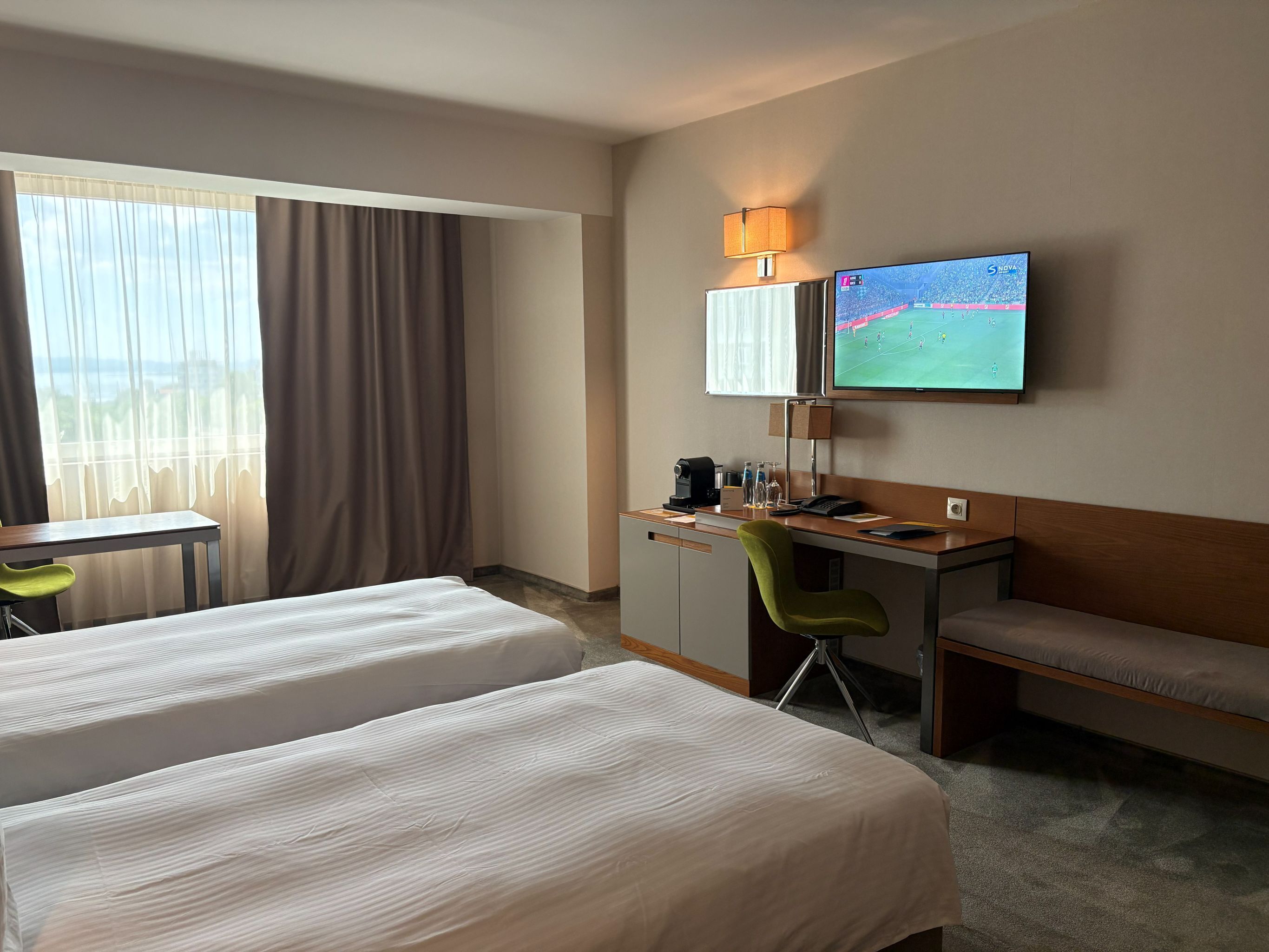 Habitación de hotel con dos camas, un escritorio, una silla, un televisor y una ventana con cortinas.