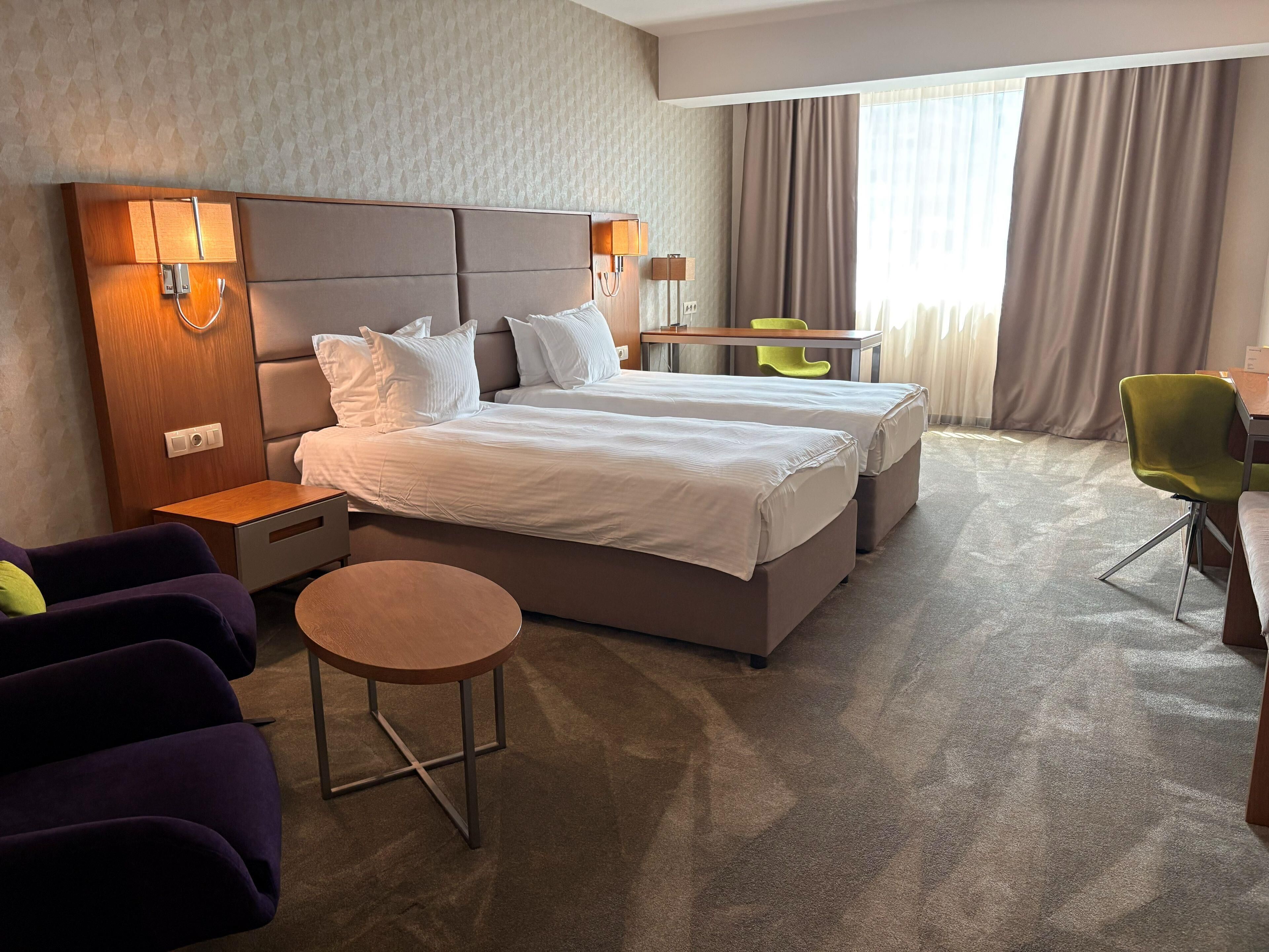 Een hotelkamer met een groot bed, nachtkastjes, een bureau, een stoel en een klein rond tafeltje.