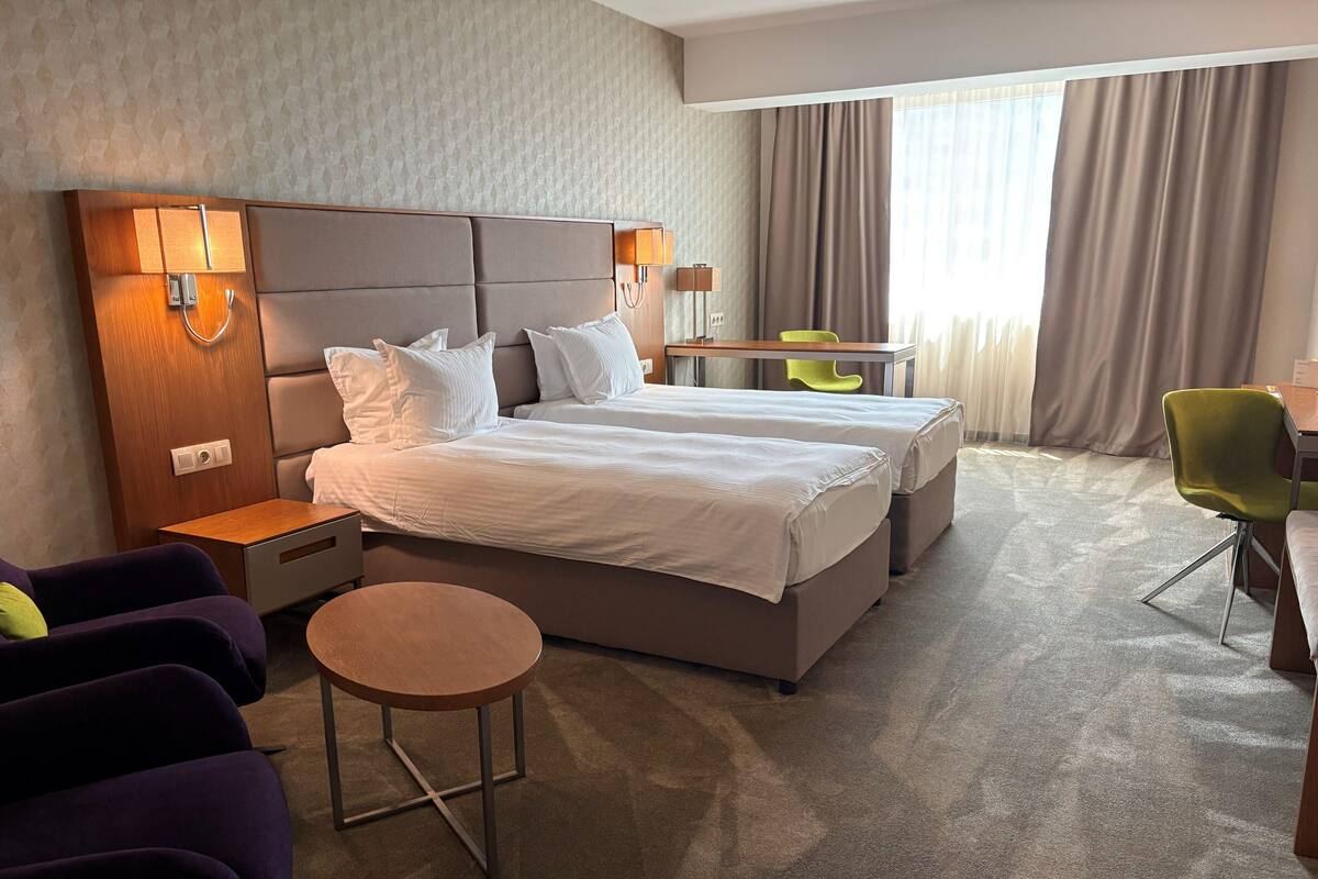 A hotel room with a large bed, bedside tables, a desk, a chair, and a small round table.