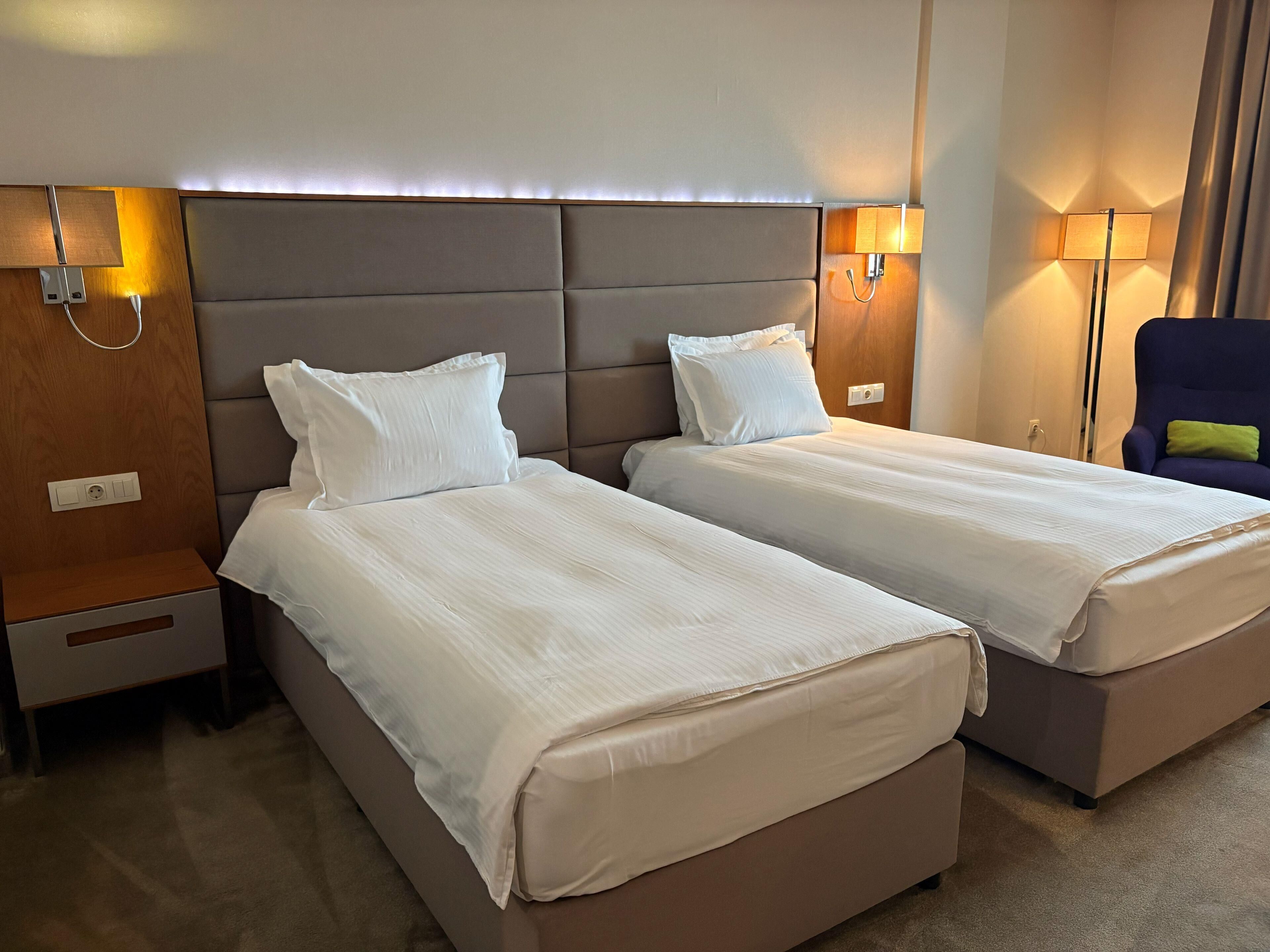 A hotel room with two beds, a wooden nightstand, a lamp, and a chair.