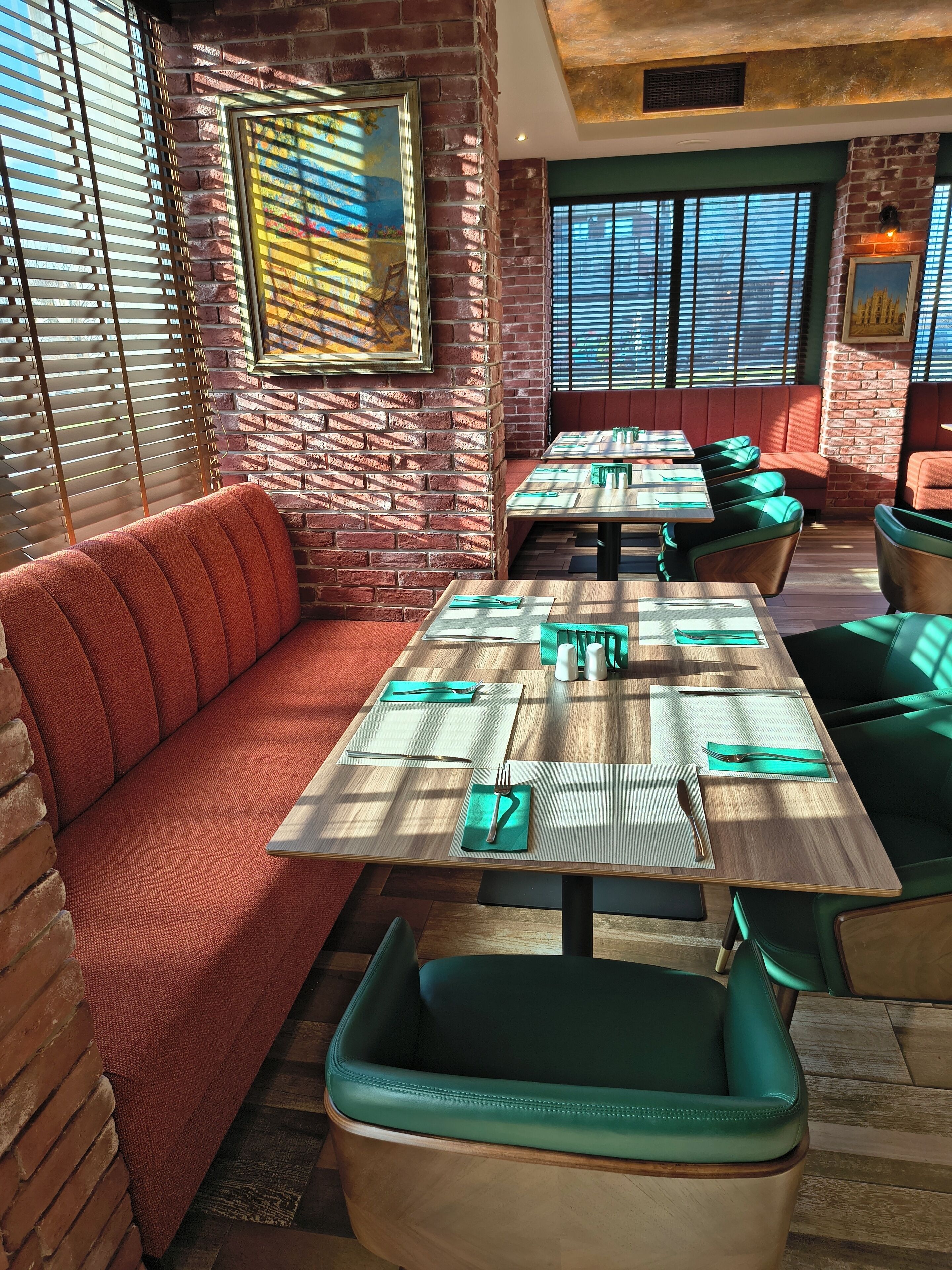 Interior de restaurante con paredes de ladrillo, asientos acolchados verdes y mesas de madera.