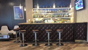 A bar area with a counter, stools, and a television screen. - Golden Tulip Varna (Varna)
