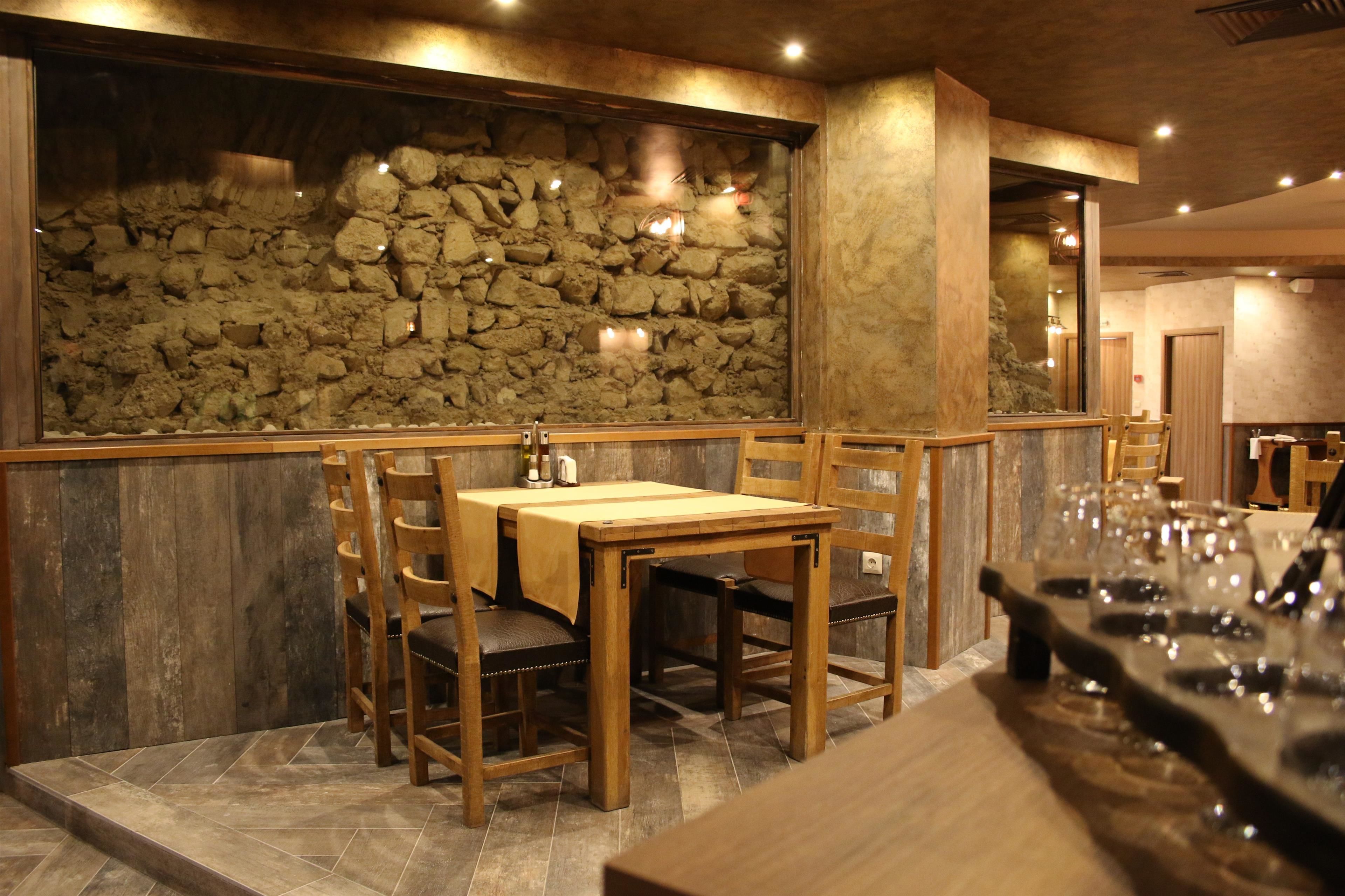 A restaurant with a stone wall backdrop, wooden tables, and chairs.