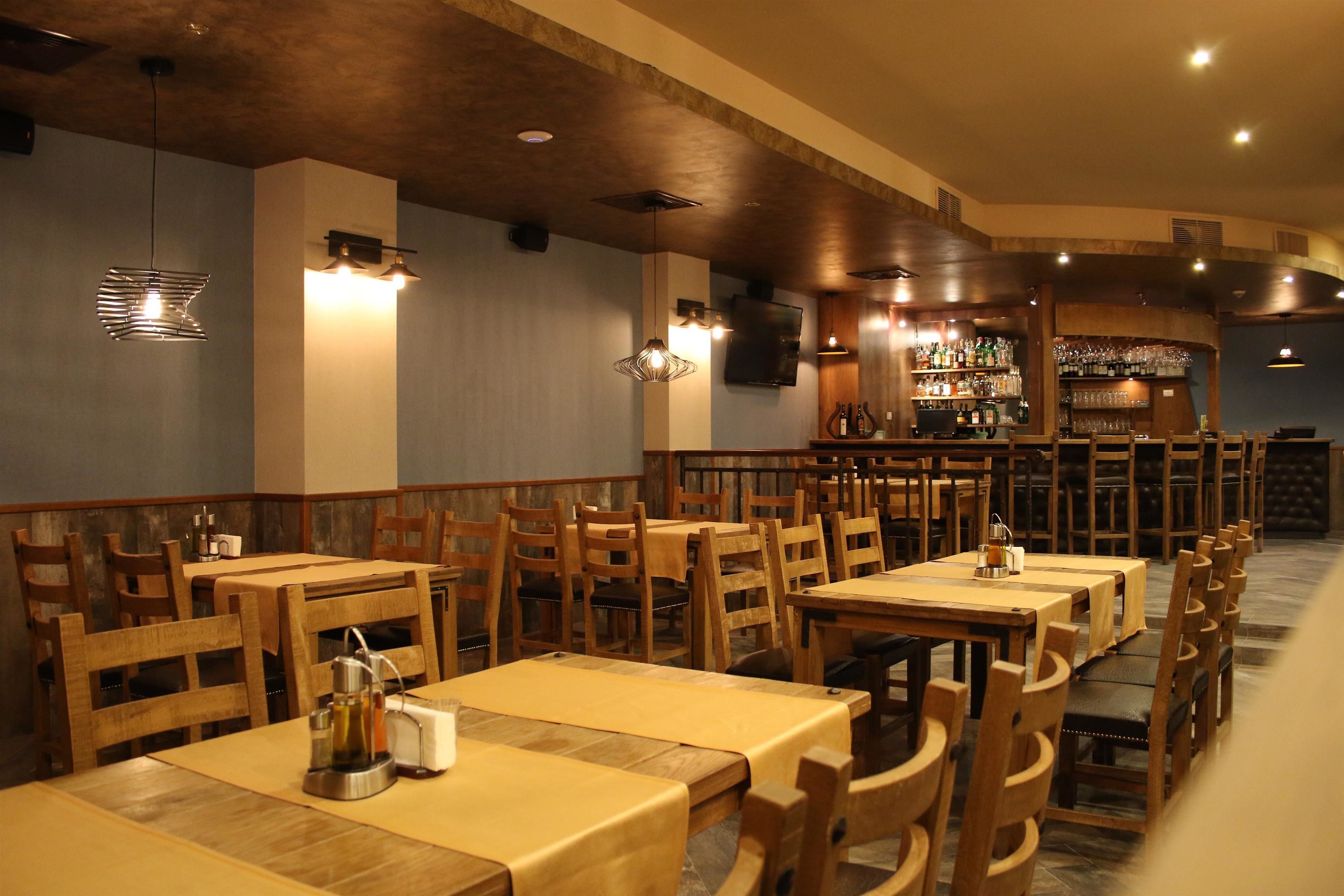 A restaurant with wooden tables and chairs, a bar area, and pendant lighting.