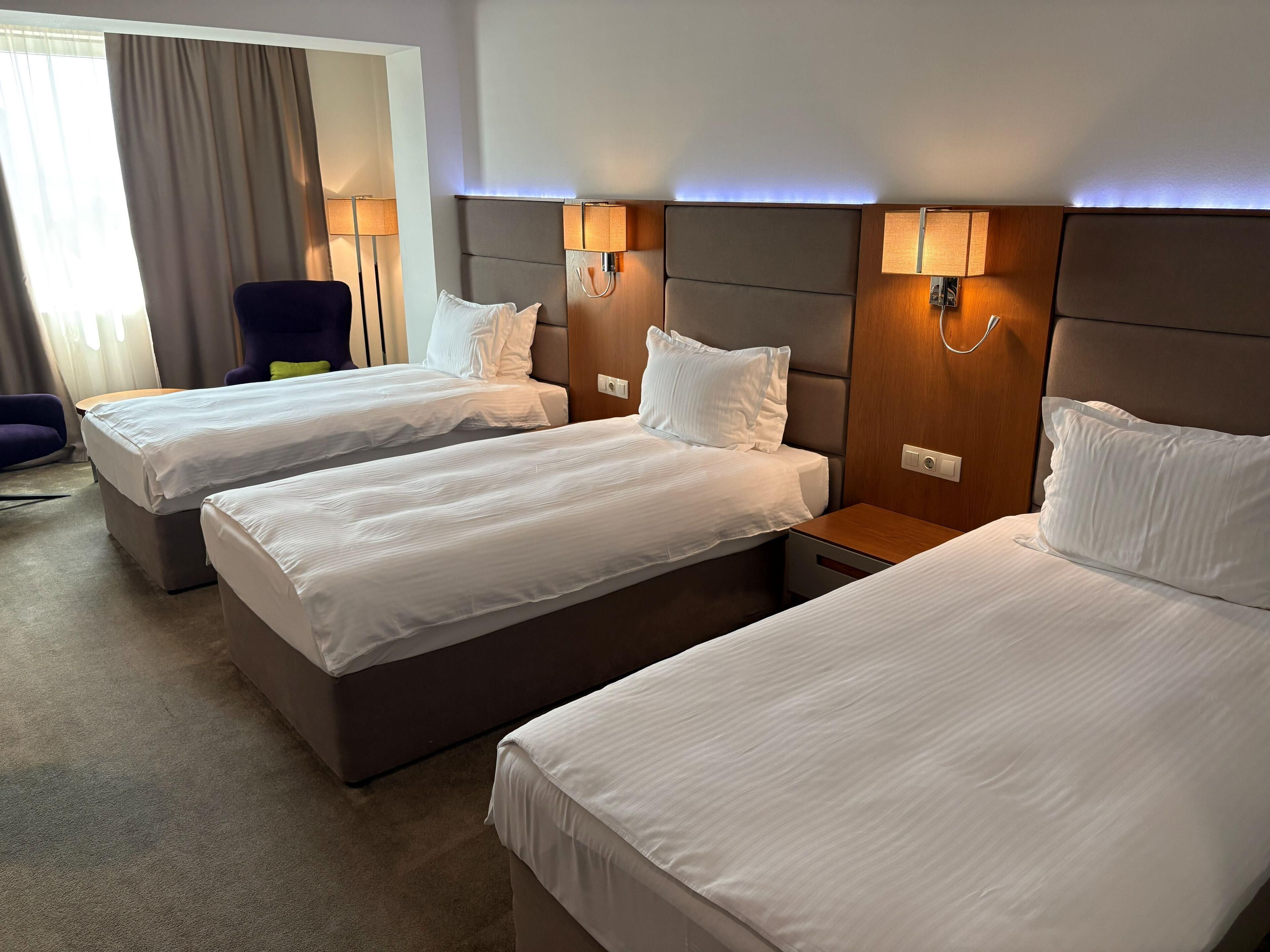 Een hotelkamer met drie bedden, een stoel en twee bedlampen.