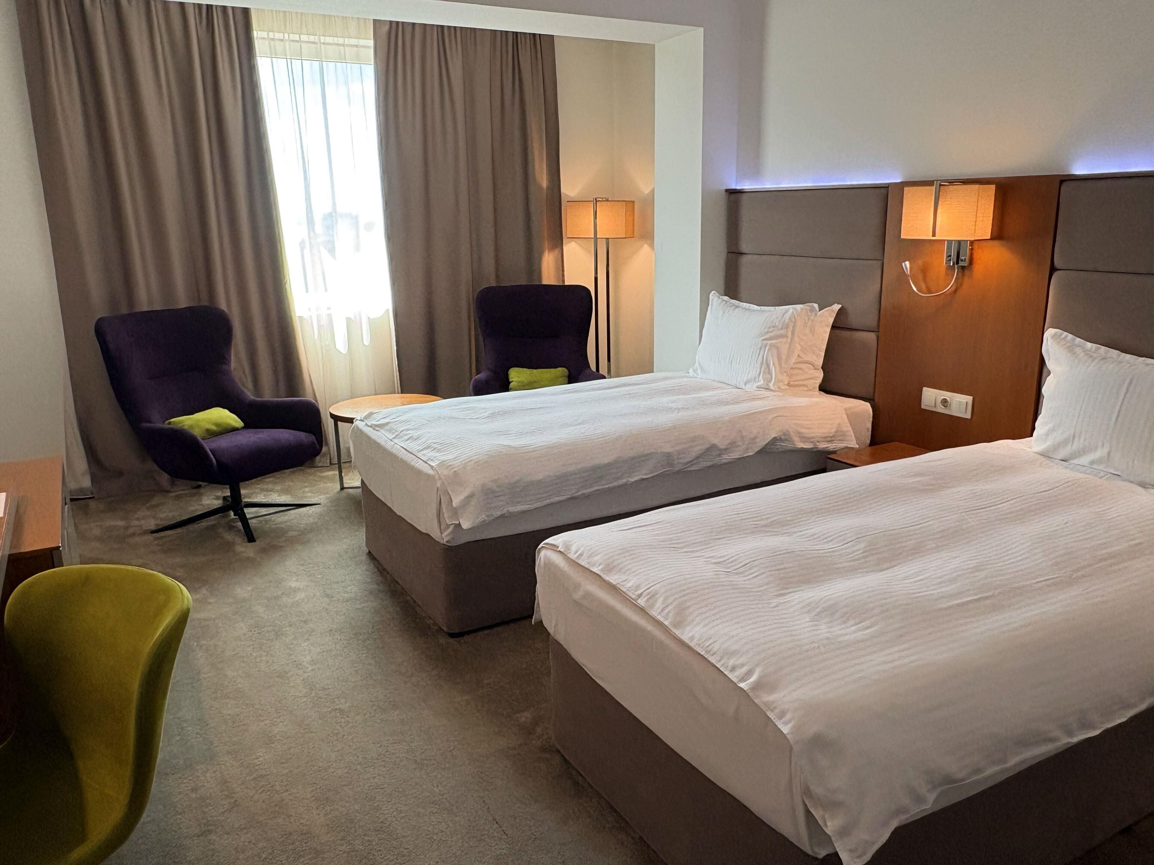 Ett hotellrum med två sängar, en stol, ett litet bord och en lampa.