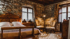 Una habitación rústica con pared de piedra, una cama con cabecera de madera, una mesita y una silla.