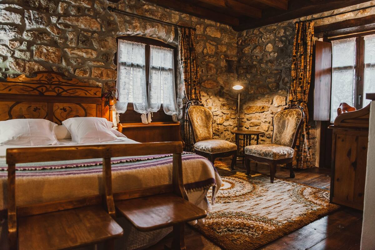 Une pièce rustique avec un mur en pierre, un lit doté d’une tête de lit en bois, une petite table et une chaise.
