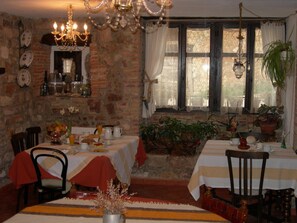 Un espace repas avec des murs en briques, un lustre et une fenêtre ornée de rideaux en dentelle.